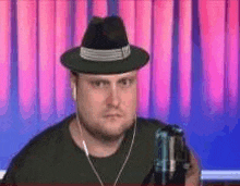 a man wearing a hat and ear buds is holding a can of beer .