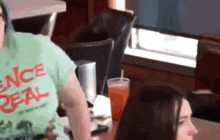 a woman wearing a green shirt that says ence deal is sitting at a table