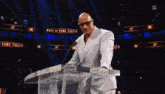 a bald man in a white suit stands at a podium with the words hall of fame 2024 behind him
