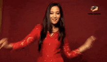 a woman in a red dress is dancing in front of a red wall .