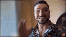 a man with a beard is smiling and wearing a shirt with a paisley print