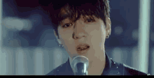 a young man is singing into a microphone while wearing a black jacket .