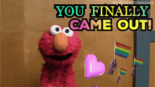 elmo from sesame street is holding a heart and rainbow flags and says you finally came out