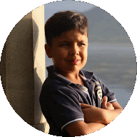 a young boy leaning against a wall with his arms crossed looking at the camera