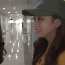 a woman wearing a green hat and a yellow shirt is smiling in a hallway
