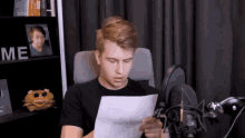 a young man sitting in front of a microphone looking at a piece of paper