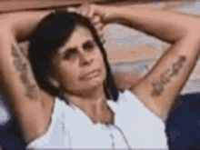 a woman with a tattoo on her arm is sitting on a bench with her arms behind her head .