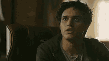 a young man with curly hair is sitting in a chair .