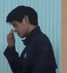 a man in a black jacket is blowing his nose with his hand .