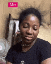 a woman is sitting in front of a fan and a sign that says me on it