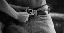 a black and white photo of a woman adjusting a man 's belt buckle .