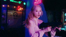 a woman in a pink sweater is holding a gun in front of a sign that says mini
