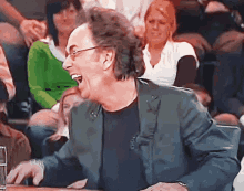 a man in a suit and glasses is laughing while sitting at a table
