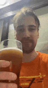 a man in an orange shirt is holding a glass of beer in his hand