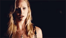 a woman with blonde hair and a necklace is making a funny face in a dark room .