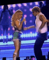 a woman singing into a microphone next to a man dancing on stage