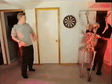 a man and a skeleton are standing in front of a dartboard