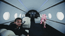 a man sits in a chair in a plane with a girl in a pink dress in the background
