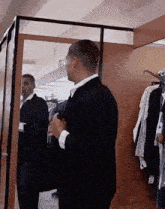 a man in a suit is standing in a dressing room looking at himself in the mirror .