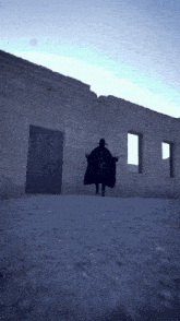 a man in a black cape and hat stands in front of a building