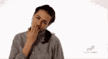 a woman in a striped shirt is holding her nose and pointing at the camera .
