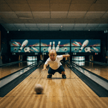 a baby crawls on a bowling alley with a bowling ball in front of him