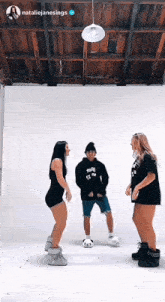 a man and two women are dancing in a room with a white wall .