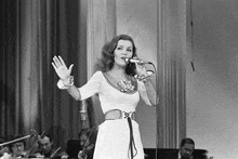 a black and white photo of a woman singing into a microphone on stage .