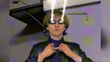a man wearing glasses and a leather jacket is adjusting his collar .