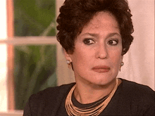 a woman wearing a necklace and earrings looks at the camera with a sad look on her face