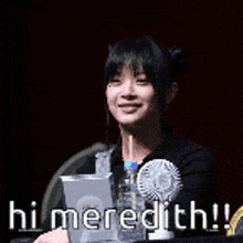 a woman is sitting at a table with a fan and a pitcher of water and says hi meredith !