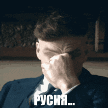 a man in a suit and tie is covering his face with his hand and the word " русня " is written below him