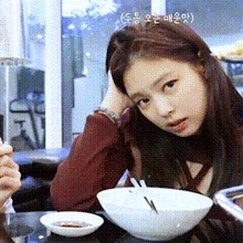 a young woman is sitting at a table with a bowl of food and chopsticks .