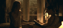 a woman is sitting on a bed reading a book to a man who is laying on a bed .