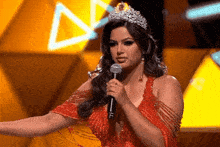 a woman in a red dress and tiara holds a microphone