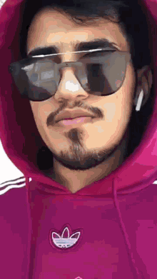 a man wearing a pink adidas hoodie and sunglasses .