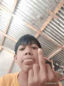 a young boy is giving the middle finger to the camera while wearing a yellow shirt .
