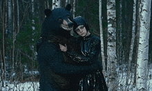 a woman in a black dress is hugging a bear in the woods .