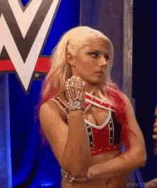 a woman with blonde hair and red hair is standing with her arms crossed in front of a wrestling logo .