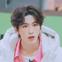 a young man in a pink shirt and white jacket is making a funny face .