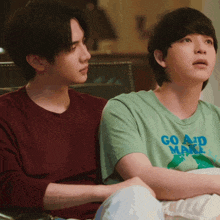 two young men are sitting next to each other one wearing a green shirt that says go and make