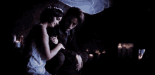 a bride and groom are sitting next to each other in a dark room with candles .