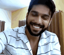a man with a beard wearing a striped shirt is smiling with his eyes closed