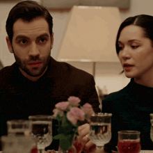 a man and woman sit at a table with wine glasses and flowers