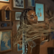 a woman with braids in her hair is standing in front of a wall with pictures on it