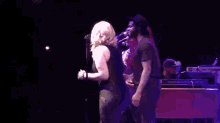 a woman in a black dress is singing into a microphone while a man in a black hat stands behind her .