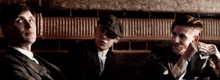 three men in suits and hats are sitting at a table talking