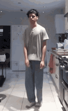 a man is standing in a kitchen wearing a grey shirt and blue pants