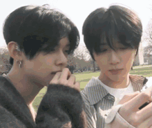 two young men are looking at a cell phone in a park