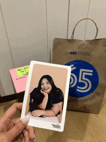 a person is holding a picture of a woman in front of a sm store bag
